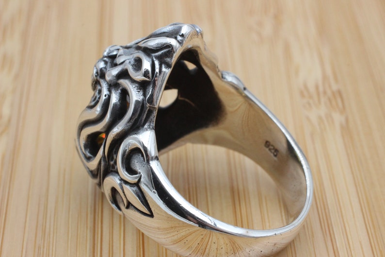 May include: A detailed sterling silver ring with an ornate design. The ring features a sculpted lion's head with intricate detailing and a polished finish. The band is marked with "925".