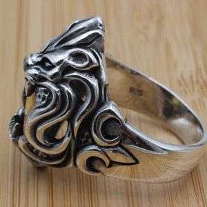 May include: A silver ring featuring a detailed lion's head design. The ring has intricate carvings and a polished finish. The band is marked with "925". This piece is a statement accessory.