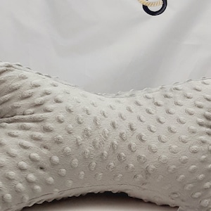 May include: A gray, textured, bow-shaped pillow with a subtle pattern of small dots. The pillow is on a white surface.