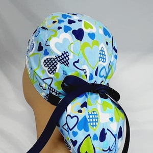 May include: A blue and white scrub hat with a heart pattern. The hat has a navy blue ribbon tie.