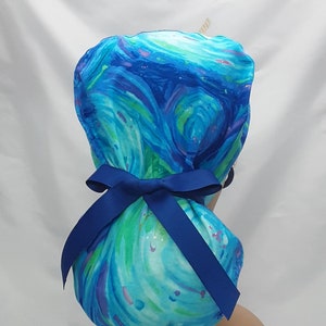 May include: Blue and green swirl patterned surgical scrub hat with a blue ribbon tied in a bow at the back.
