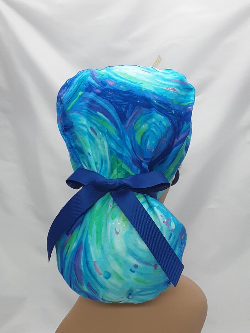 May include: Blue and green swirl patterned surgical scrub hat with a blue ribbon tied in a bow at the back.