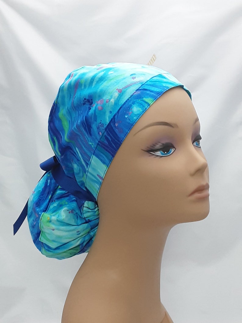 May include: A blue and green patterned surgical scrub hat with a blue ribbon tie. The hat is made of a soft, comfortable fabric and is designed to be worn by medical professionals.