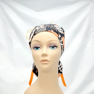 Pode incluir: Um gorro cir&uacute;rgico estampado em preto e branco com detalhes em laranja. O gorro tem duas fitas longas de cor laranja.