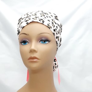 May include: A white and brown leopard print surgical scrub hat with pink ties. The hat is made of a soft, comfortable fabric and is designed to be worn by medical professionals.