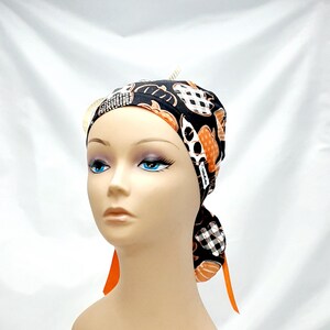 Pode incluir: Um gorro cir&uacute;rgico preto e laranja estampado com uma gravata xadrez preta e branca. O gorro tem um pequeno enfeite de strass.