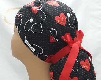 May include: Black scrub hat with red hearts and a stethoscope pattern. The hat has a red ribbon tied on the back.