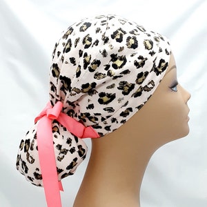 May include: A pink and gold leopard print surgical scrub hat with a pink ribbon ponytail holder.