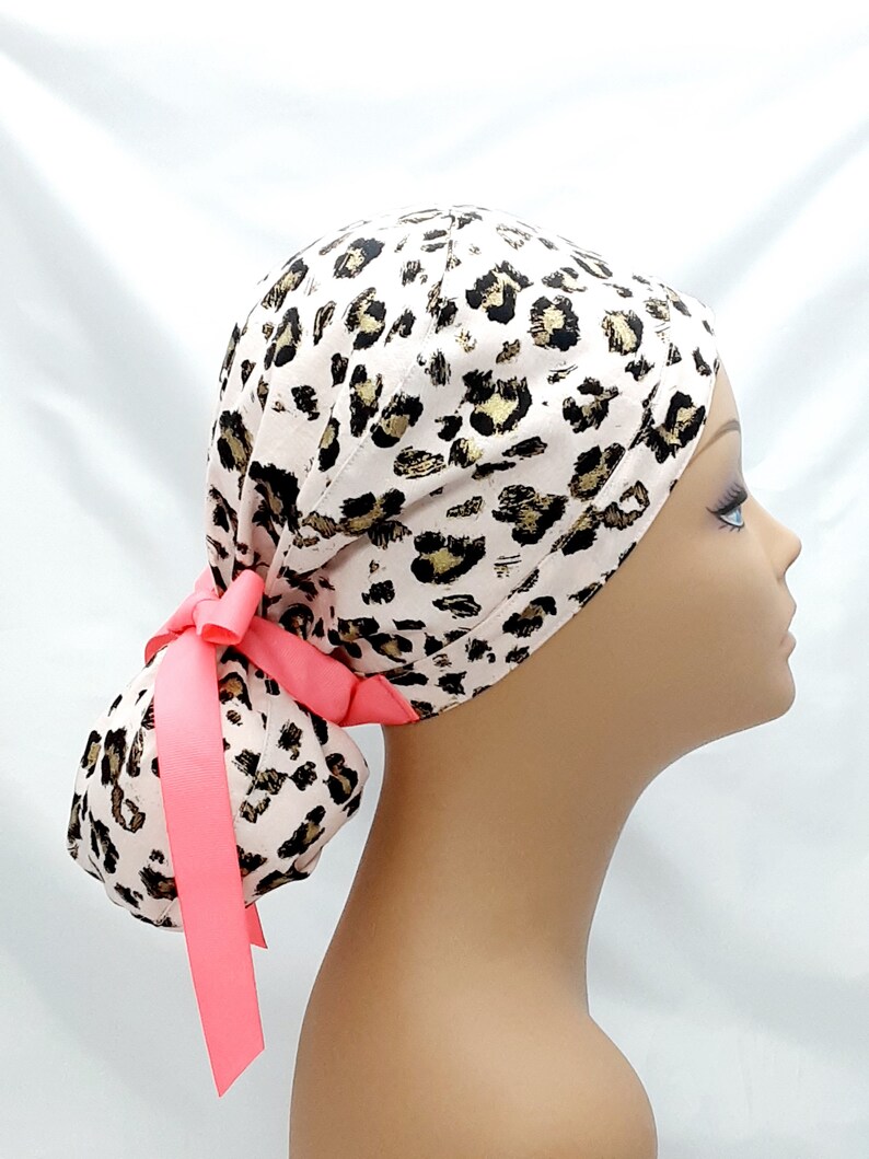 May include: A pink and gold leopard print surgical scrub hat with a pink ribbon ponytail holder.
