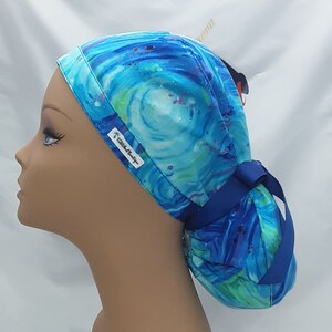 May include: A blue and green patterned surgical scrub hat with a blue ribbon tie. The hat has a white label with the text "Scrub Star" on it.
