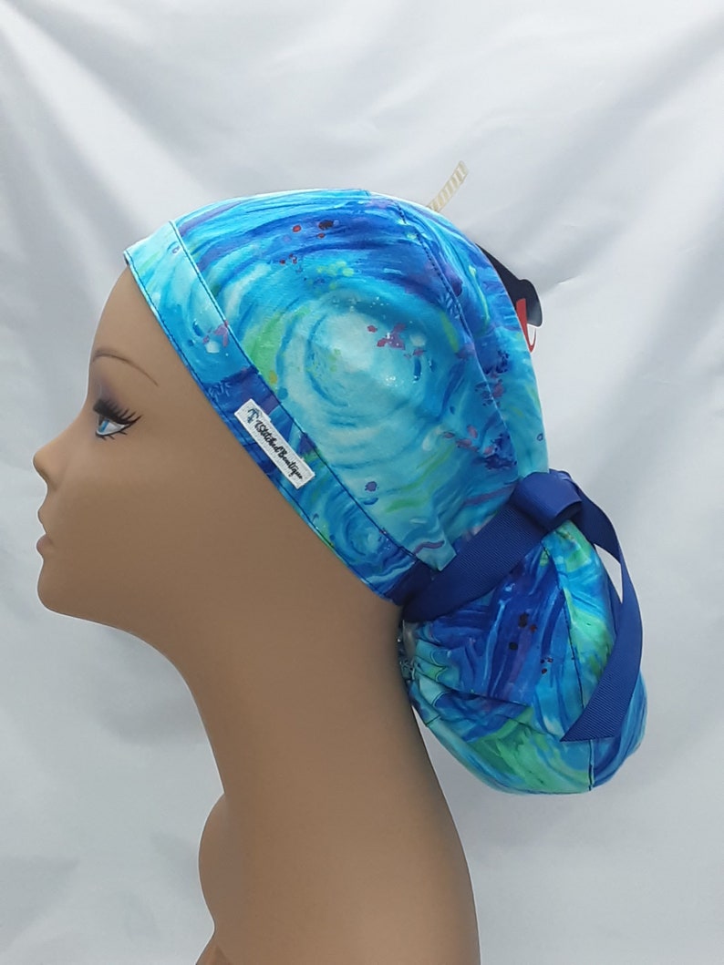 May include: A blue and green patterned surgical scrub hat with a blue ribbon tie. The hat has a white label with the text "Scrub Star" on it.