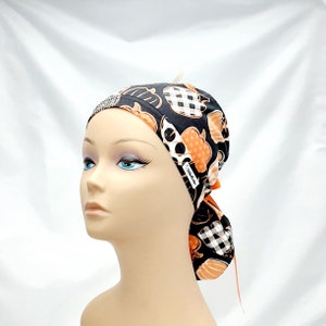 Pode incluir: Um gorro de cirurgia preto e branco com ab&oacute;boras laranja e um la&ccedil;o branco. O gorro tem um pequeno strass na frente.