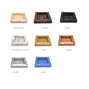 May include: A collection of eight square wooden trays arranged in a grid, featuring various finishes labeled as unfinished, stained, black, distressed white, gold, copper, silver, and blue. Each tray has a raised border and a recessed center.
