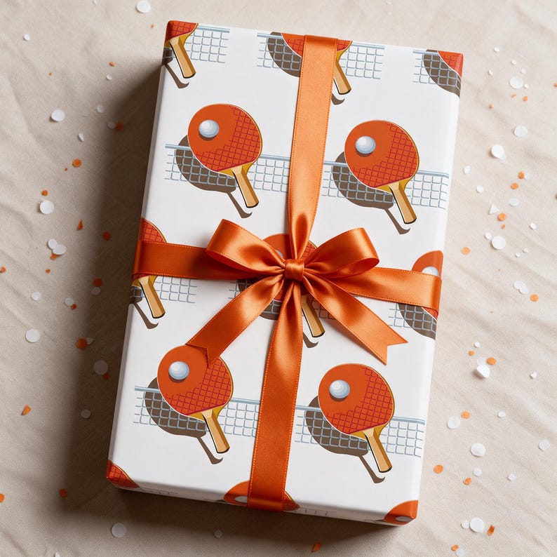 May include: A rectangular gift box wrapped in white paper featuring a repeating pattern of orange table tennis paddles, white balls, and light blue nets. The package is tied with a smooth, vibrant orange satin ribbon tied in a centered bow.