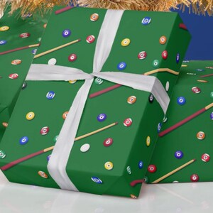 May include: Green gift boxes wrapped in paper with a pool table design. The wrapping paper features billiard balls, cues, and white chalk spots. A white ribbon is tied around the boxes.