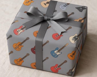 Puede incluir: Una caja de regalo cuadrada envuelta en papel gris con un patrón repetitivo de varias guitarras eléctricas y acústicas en colores rojo, azul, naranja y crema, atada con un lazo de cinta de satén gris oscuro ancho en la parte superior.