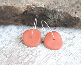 May include: A pair of terracotta clay earrings with a simple, organic shape. The earrings are suspended from silver hoops.