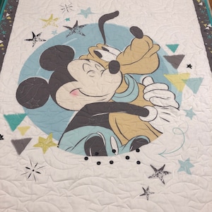 May include: A white quilted baby blanket with a blue and gray circle featuring Mickey Mouse and Pluto. The circle is surrounded by stars and triangles in shades of gray, blue, and yellow. The blanket has a gray and teal border with stars and triangles.