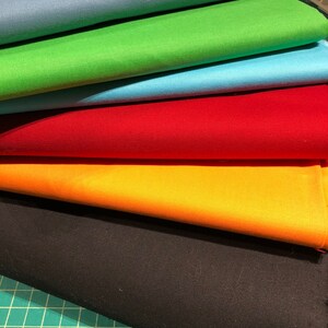 May include: A stack of six fabric swatches in different colors, including black, orange, red, blue, green, and light blue. The fabric is folded and arranged in a rainbow pattern.