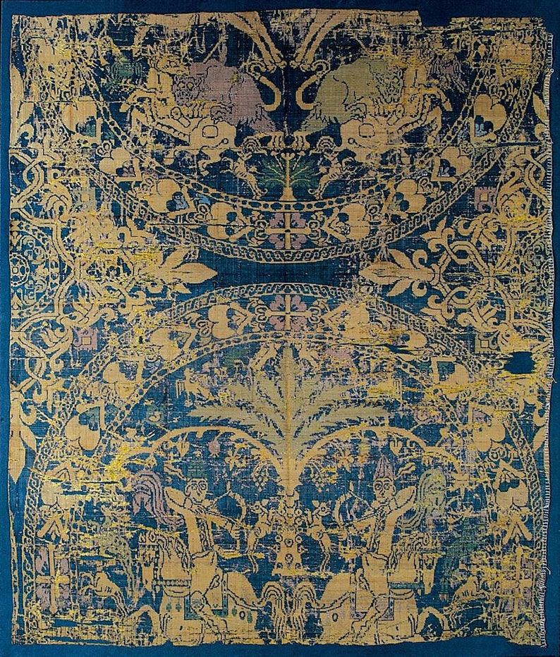 May include: A fragment of a blue and gold silk tapestry featuring a repeating pattern of stylised trees, flowers, and geometric designs. The tapestry is woven with intricate details and features a central motif of a tree with a crown.