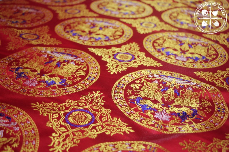 May include: Red fabric with a repeating pattern of gold and blue embroidered circles. Each circle features a stylised design of two mythical creatures with wings and tails. The fabric has a subtle sheen and a luxurious feel.