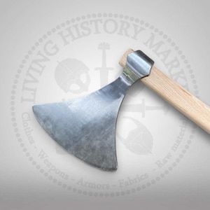 Könnte beinhalten: Eine Handaxt mit einer breiten, geschwungenen, silberfarbenen Metallklinge mit glatter, polierter Oberfläche. Die Klinge ist sicher an einem hellen, geraden Holzgriff befestigt, der diagonal von oben rechts durch den Bildausschnitt verläuft.