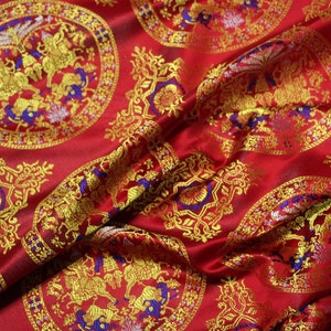 May include: Red fabric with a repeating pattern of gold and blue circular designs. The designs feature stylised animals and floral motifs.