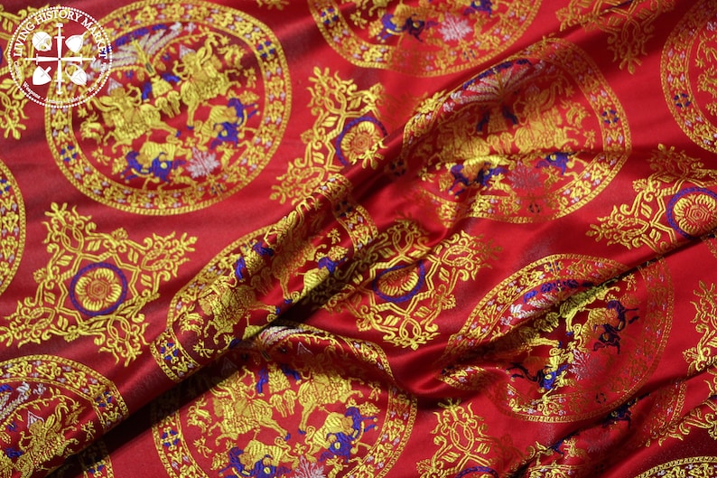 May include: Red fabric with a repeating pattern of gold and blue circular designs. The designs feature stylised animals and floral motifs.