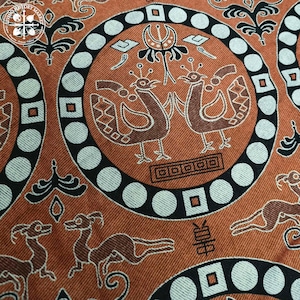 Può includere: Primo piano di un tessuto fantasia con un motivo ripetuto. Il tessuto presenta motivi circolari con uccelli stilizzati e forme geometriche in marrone, nero e bianco. Il tema generale è un tessuto etnico o vintage.