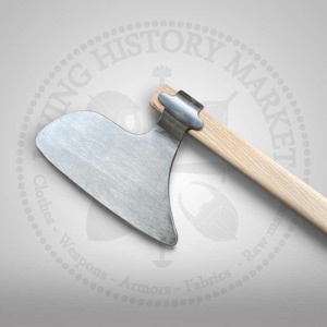 Puede incluir: Una cabeza de hacha de metal con una hoja ancha y curva de acabado plateado, fijada firmemente a un mango de madera clara. El hacha presenta un filo distintivo y ensanchado, con un casquillo metálico donde el mango se une a la cabeza.