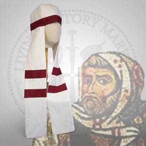 Może przedstawiać: Biały średniowieczny kaptur z bordową opaską i paskami. Kaptur jest prezentowany na głowie manekina. Projekt charakteryzuje się długimi, płynącymi panelami z bordowymi paskami, oferując historyczną estetykę. Kaptur jest wykonany z jasnej tkaniny.