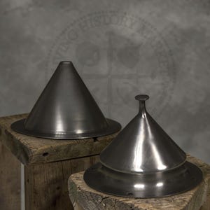 May include: Two metal conical objects with a circular base sit on a wooden surface. One is a simple cone, the other has a rounded top with a small knob. The objects are a dark, metallic color, likely steel.