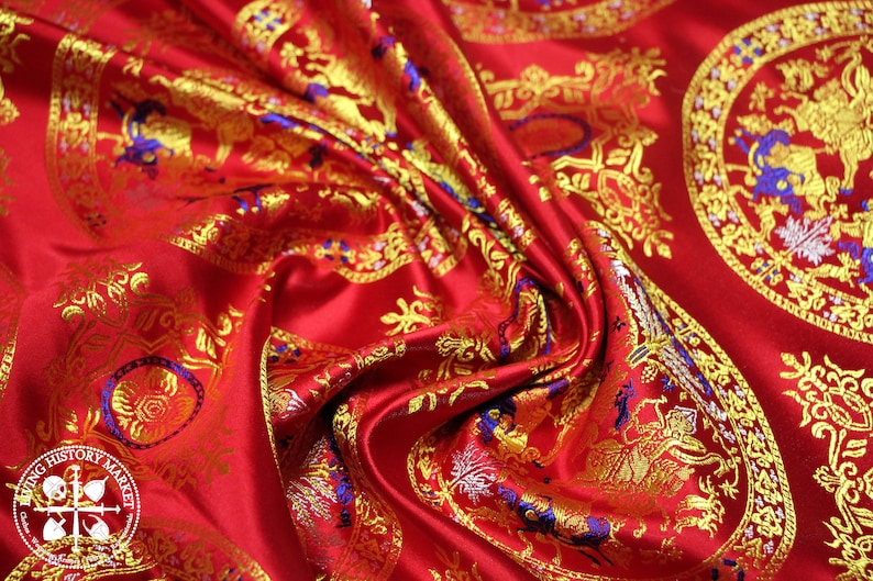 May include: Red fabric with a gold and blue brocade pattern. The pattern features repeating circular designs with intricate details.