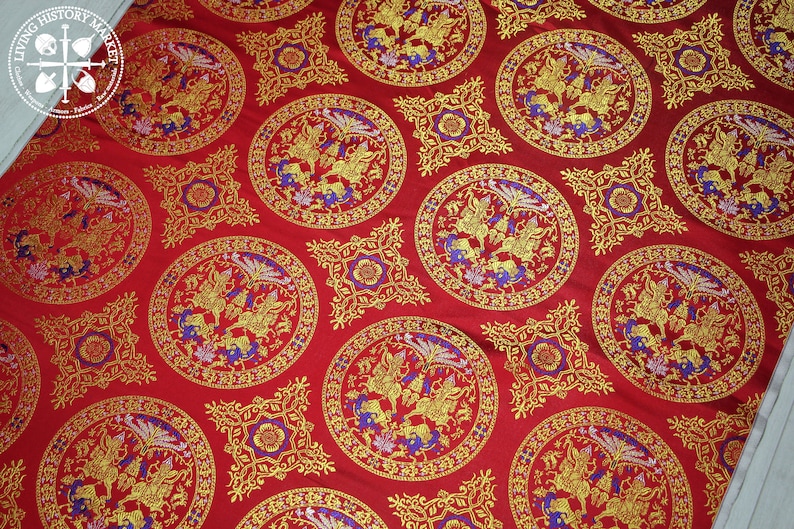 May include: Red fabric with a repeating pattern of gold and blue circular designs. Each circle features a stylised bird design with intricate details.