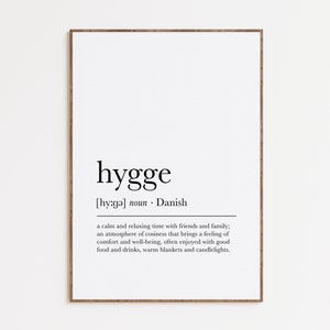 May include: A black and white printable poster with the word "hygge" in a large font, followed by its pronunciation and definition. The definition describes hygge as a Danish concept of a cozy and relaxing time with friends and family, often enjoyed with good food and drinks.