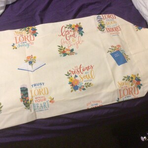 May include: A cream-colored fabric runner featuring a repeating pattern of floral arrangements and religious text including "Sing to the Lord," "Love God love & people," "He restores my soul," and "Trust in the Lord with all your heart."
