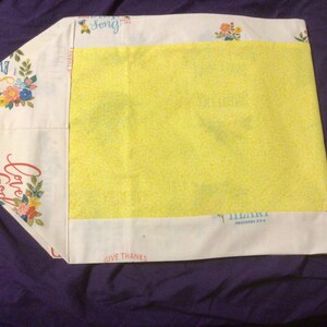 May include: A rectangular fabric pillowcase featuring a cream-colored background with floral patterns and text including "Love God," "Give Thanks," and "Song." A large, bright yellow panel is centered on the front, contrasting with the printed borders.
