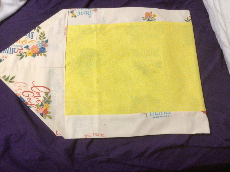 May include: A rectangular fabric pillowcase featuring a cream-colored background with floral patterns and text including "Love God," "Give Thanks," and "Song." A large, bright yellow panel is centered on the front, contrasting with the printed borders.