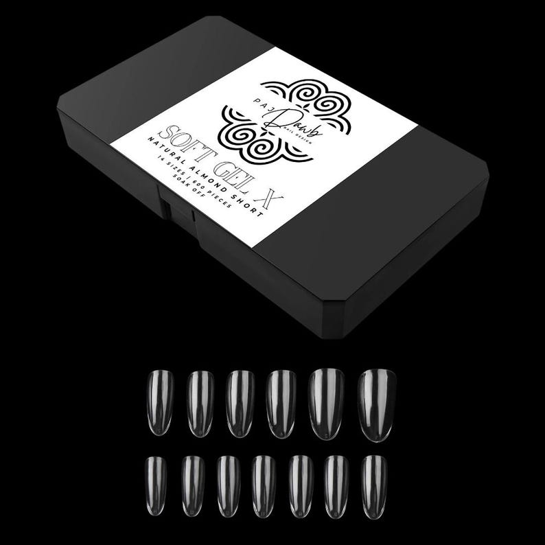 May include: A black box of natural almond short soft gel X nail tips. The box has a white label with the text "PAJ D'Amour Nail Design" and "SOFT GEL X". Below the box are 14 clear nail tips.
