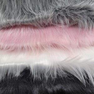 May include: Close-up of four layers of faux fur fabric in shades of gray, pink, white, and black. The fur has a long, soft pile, creating a textured and luxurious appearance. Ideal for craft projects, fashion, or home decor.
