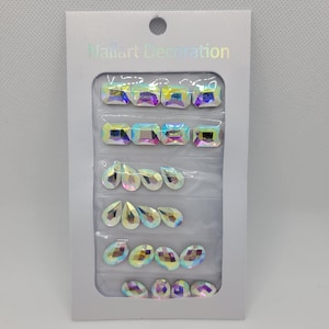 May include: A package of iridescent nail art decorations. The package contains a variety of shapes, including squares, ovals, and teardrops. The package is labeled "Nailart Decoration".
