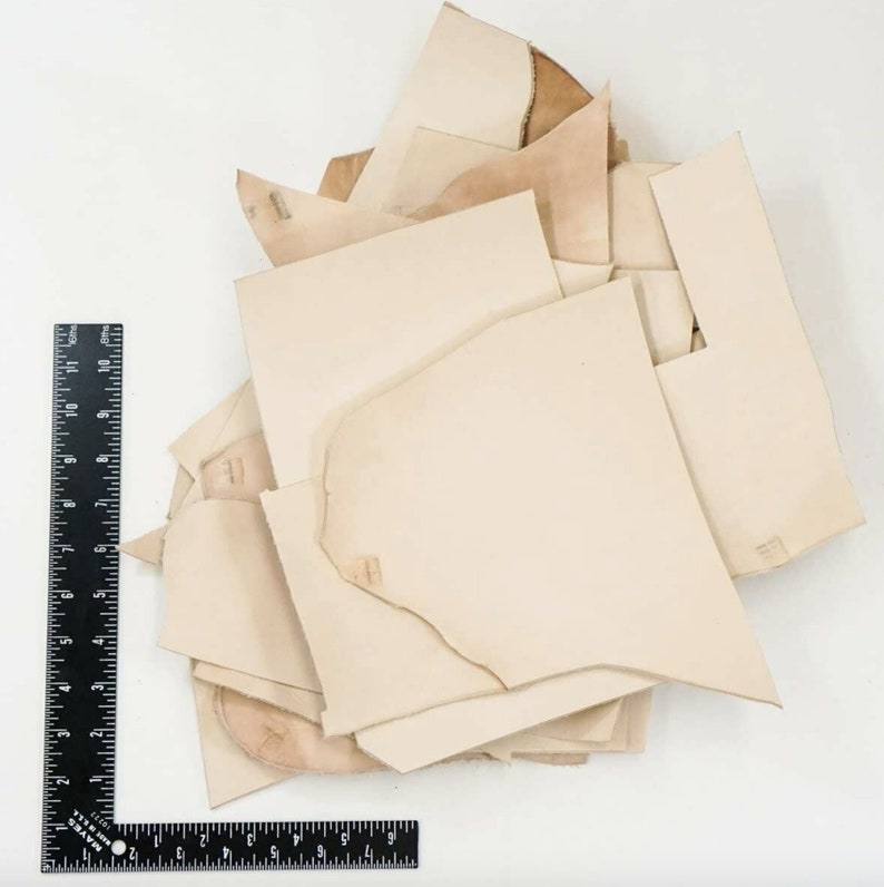 May include: A pile of off-white leather scraps of various sizes and shapes. A black ruler is in the lower left corner of the image.
