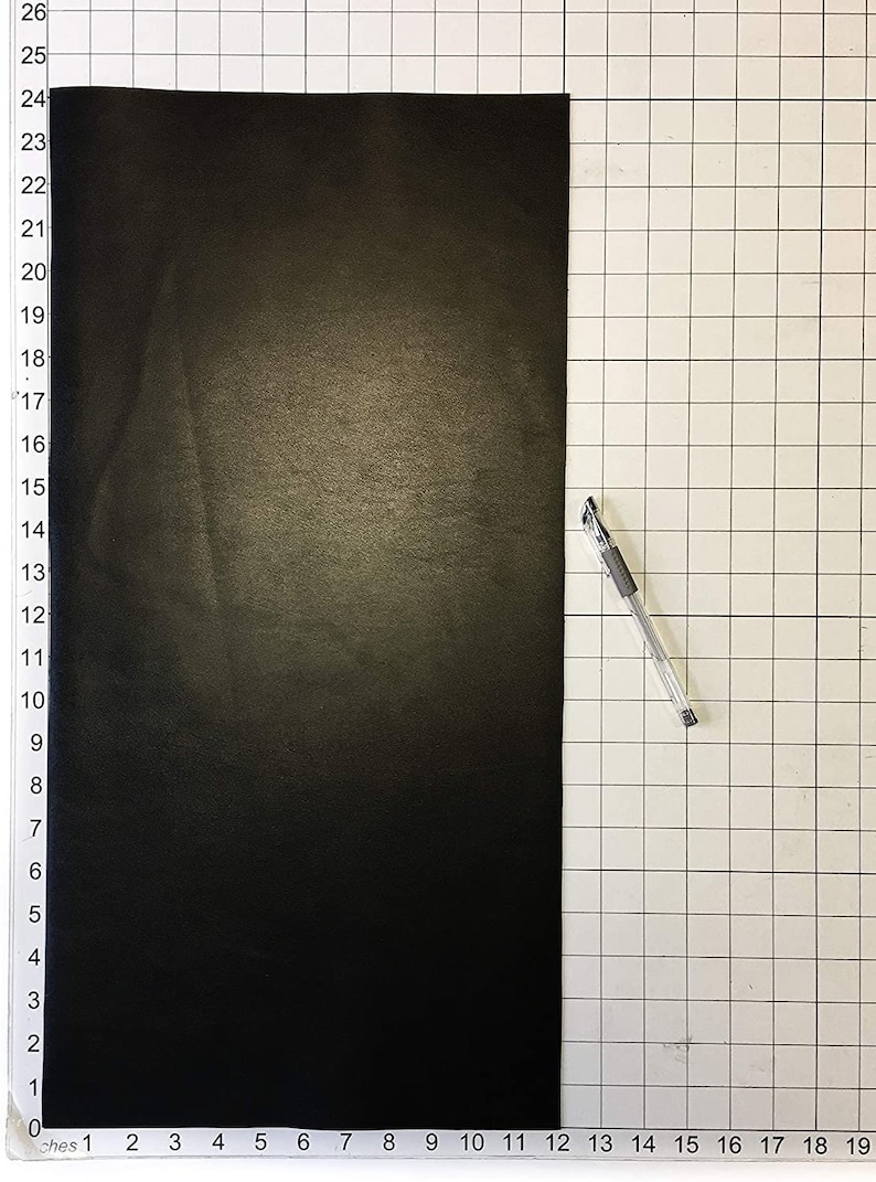 Może przedstawiać: Czarny arkusz materiału o wymiarach 63,5 cm x 48,3 cm, rozłożony na białym tle z siatką. Srebrny długopis leży na siatce po prawej stronie arkusza.