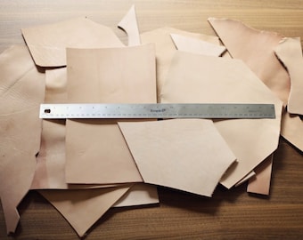 May include: A pile of light brown leather scraps of various sizes and shapes. A metal ruler is placed on top of the leather scraps. The ruler is marked with inches and has the word "Empire" printed on it.
