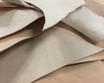 Pode incluir: Vista de perto de várias peças de couro de cor natural. As peças de couro, de formas irregulares, apresentam texturas variadas, desde lisas a camurçadas. As cores variam do bege claro ao castanho claro.