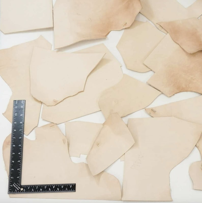 May include: A collection of off-white leather scraps of various sizes and shapes. The leather is smooth and appears to be of good quality.