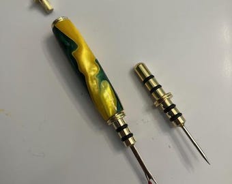 May include: A sewing seam ripper with a yellow and green marbled handle and a gold-colored metal tip. A smaller, matching tool and a chain with a gold-colored pendant are also present. The tools are designed for removing stitches.