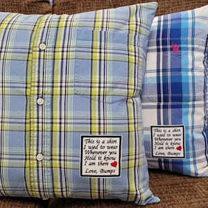 May include: Three plaid pillows made from repurposed shirts. The pillows feature blue, green, and white plaid patterns. Each pillow has a patch with text that reads "This is a shirt I used to wear..." and a heart. The pillows are on a brown couch.