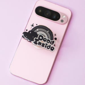 May include: A black and silver phone ring holder with a rainbow and cloud design. The text "Dead Inside" is written in black on the holder.