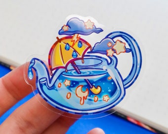 May include: A blue teapot with a yellow umbrella inside, surrounded by clouds, stars, and a crescent moon. The teapot is filled with blue liquid and has a white rim.